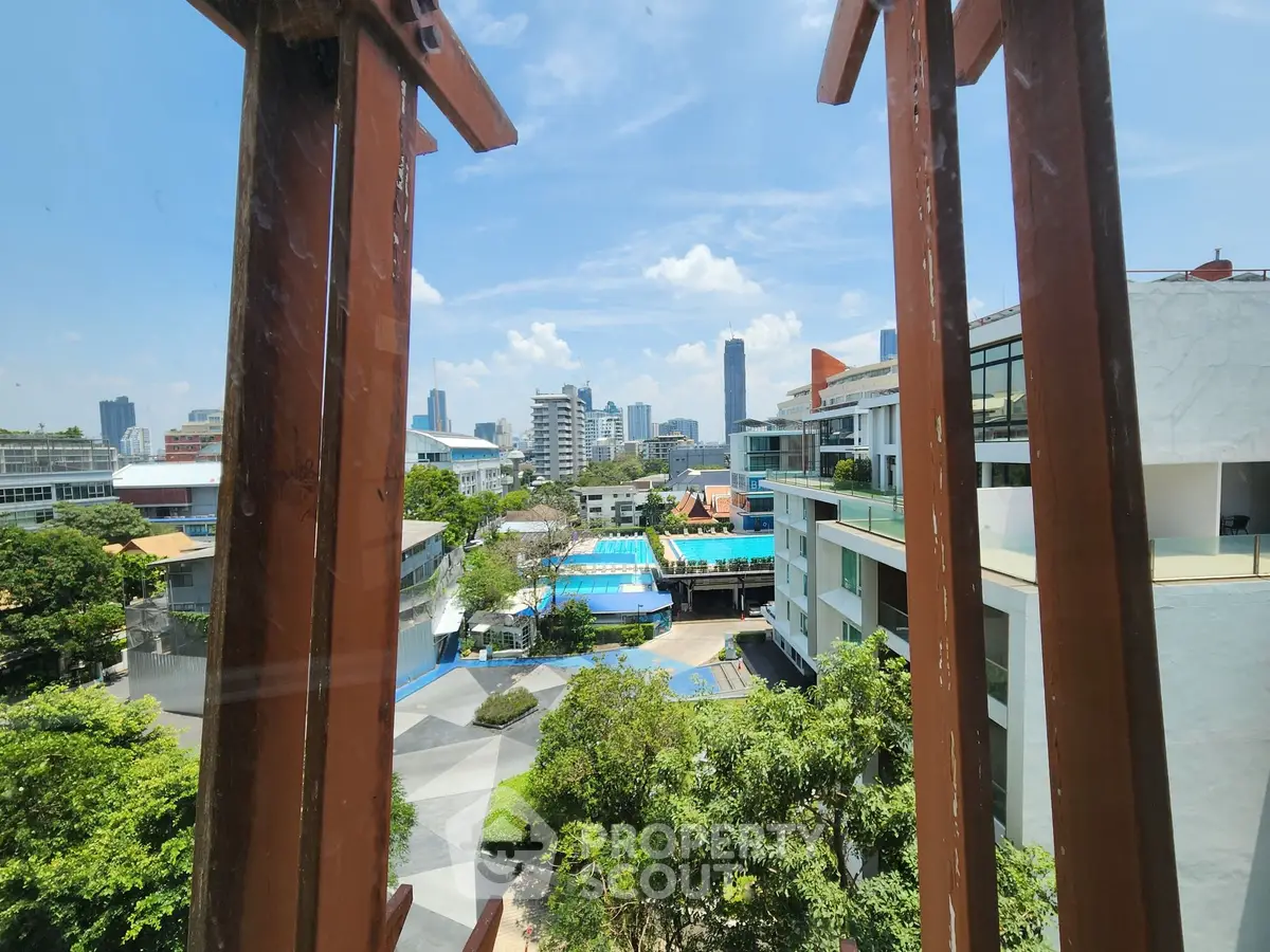 Stunning city view from a modern apartment window with lush greenery and pool