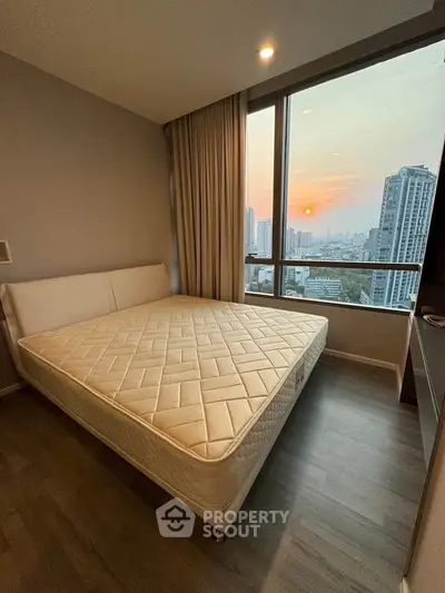 Modern bedroom with large window offering stunning city view at sunset.