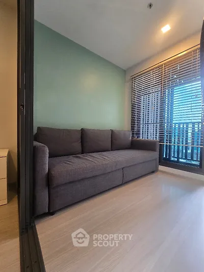 Modern living room with sleek sofa and large window offering city view.