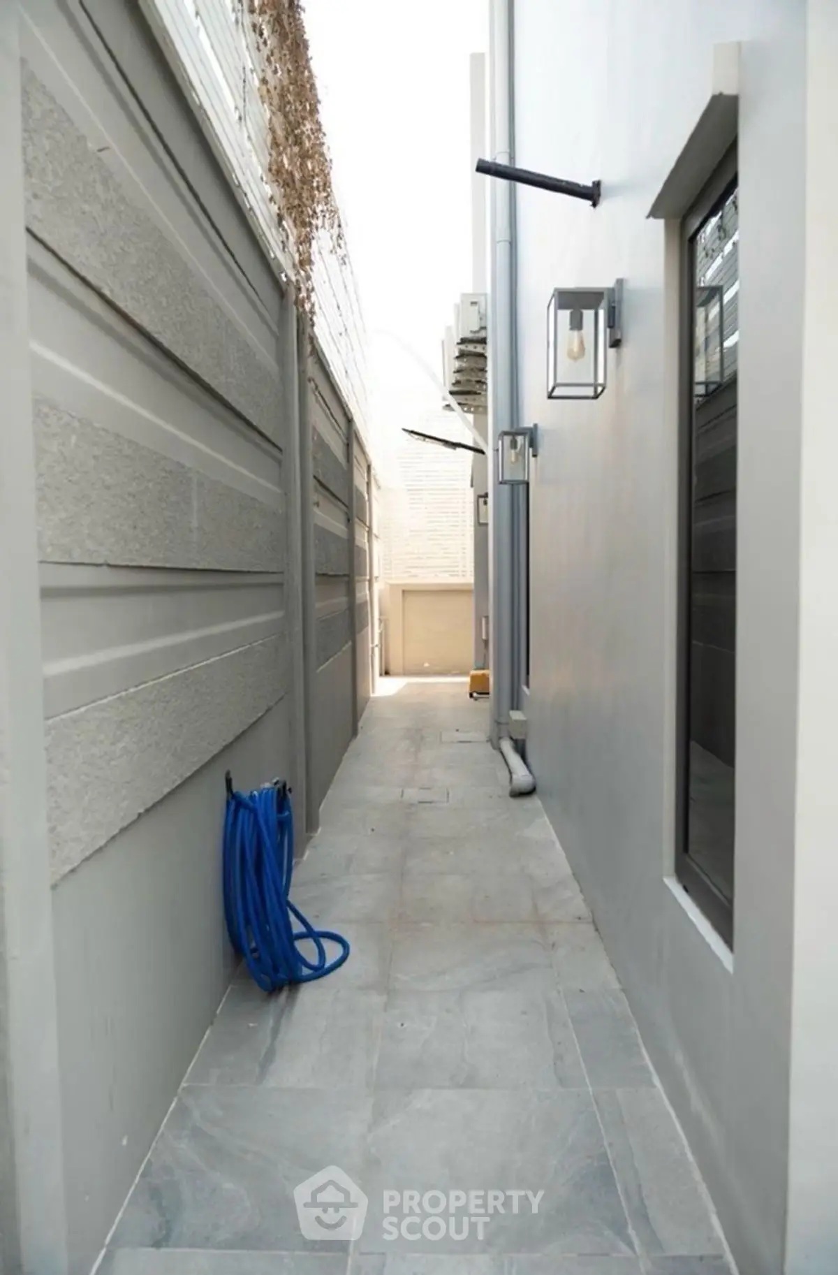 Narrow exterior passageway with modern lighting and hose, ideal for urban homes.