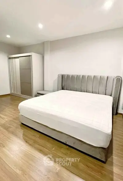 Spacious modern bedroom with elegant bed and sleek wardrobe on wooden flooring.