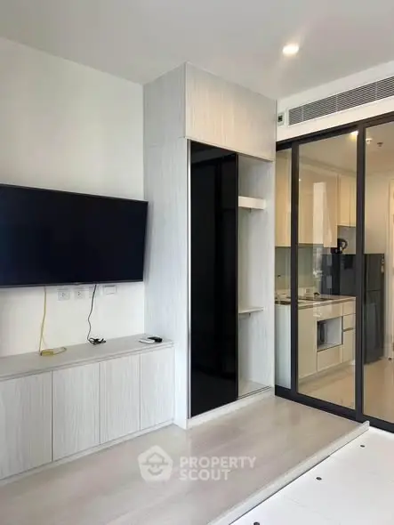 Modern living room with sleek TV setup and glass partition leading to a stylish kitchen.
