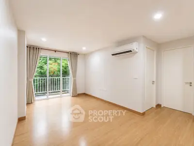 Spacious empty living room with balcony and air conditioning, featuring wooden flooring and bright natural light.