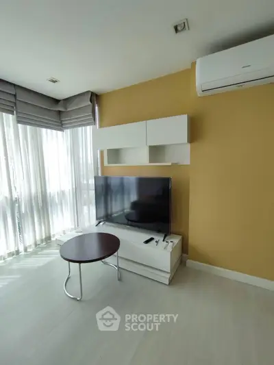Modern living room with large TV, air conditioning, and natural light from floor-to-ceiling windows.