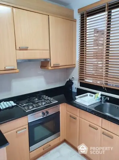 Modern kitchen with wooden cabinets, gas stove, and sleek black countertops.