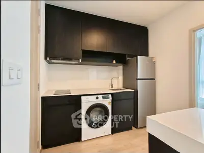 Modern kitchen with sleek black cabinets, integrated washing machine, and stainless steel fridge.