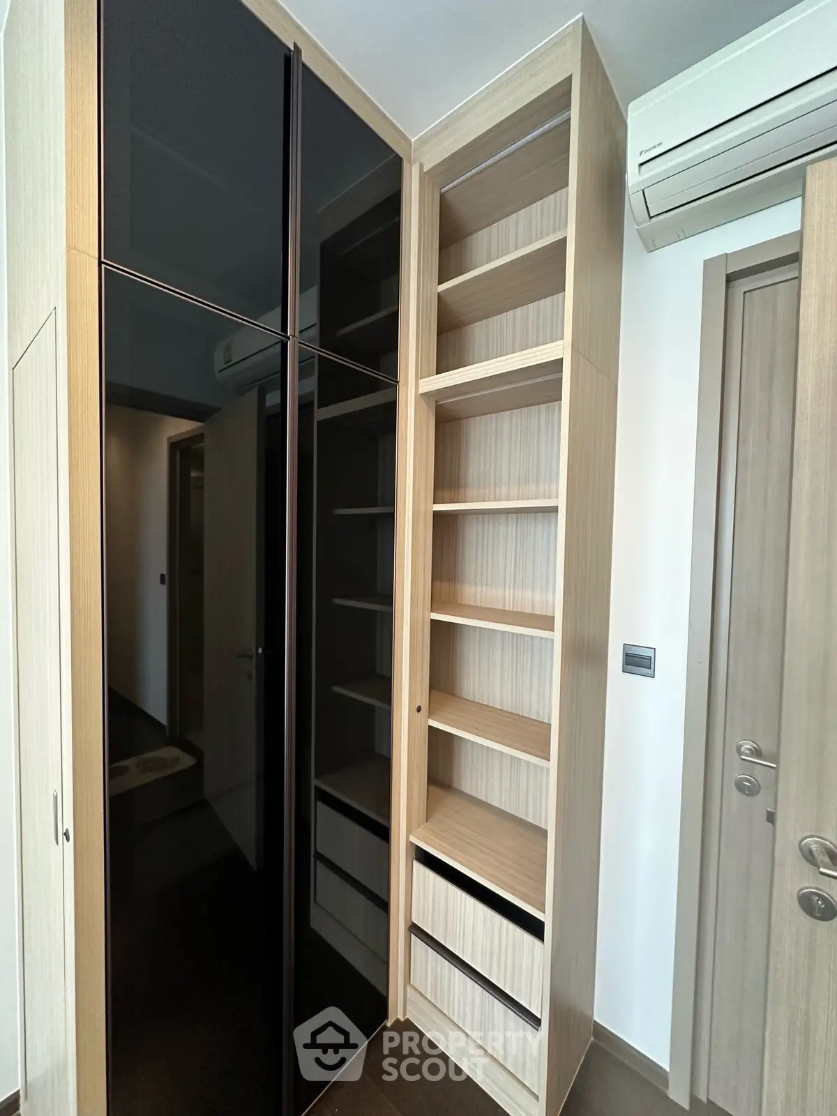 Modern storage space with sleek black glass doors and wooden shelving in a contemporary apartment.