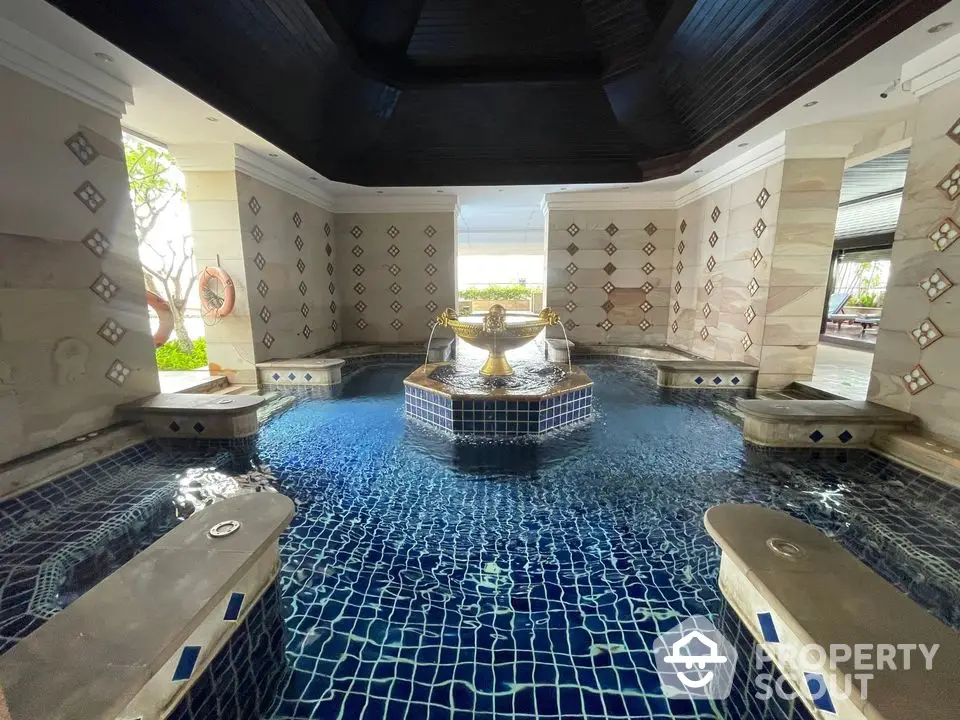 Luxurious indoor pool with elegant tile design and central fountain in upscale property