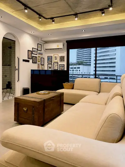 Stylish living room with modern decor, large beige sectional sofa, and urban view through wide windows.