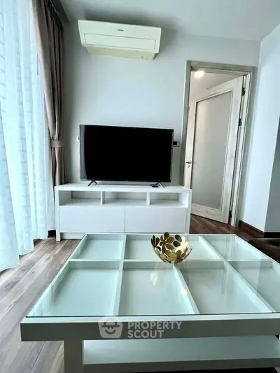 Modern living room with glass coffee table and TV unit, featuring elegant decor and natural light.