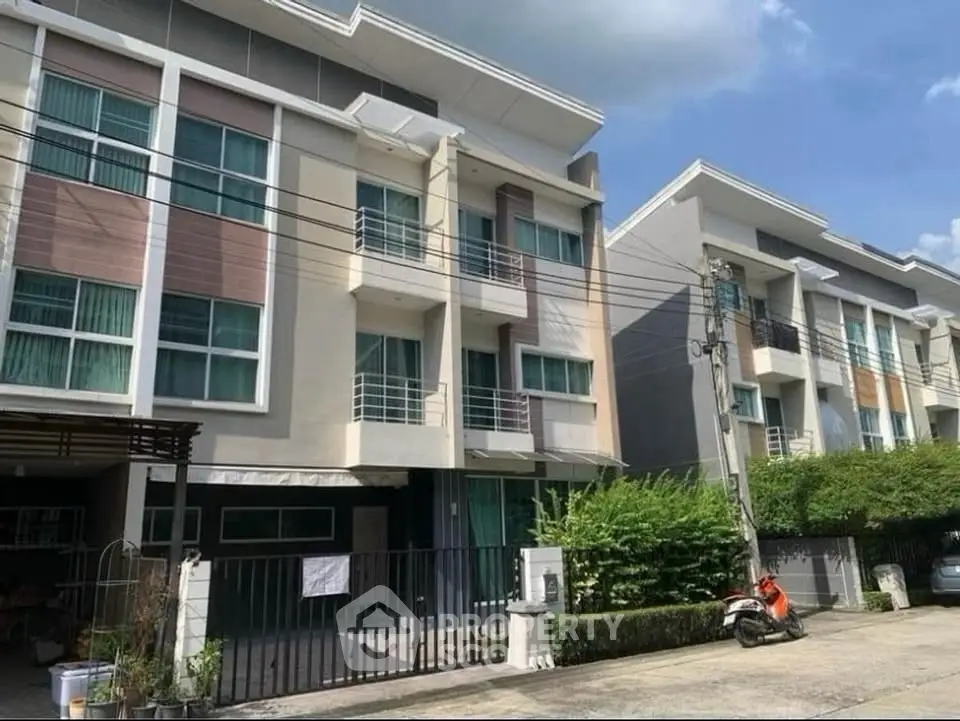 Modern multi-story residential building with balconies and gated entrance in a suburban neighborhood.
