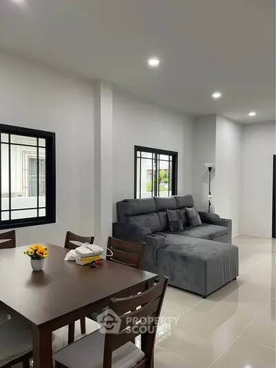 Modern living room with sleek gray sofa and dining area, bright and spacious interior.