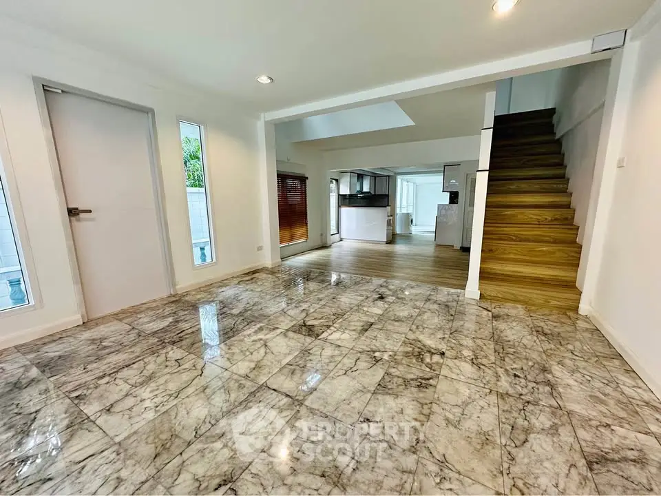 Spacious modern living area with marble flooring and wooden staircase in a stylish home.