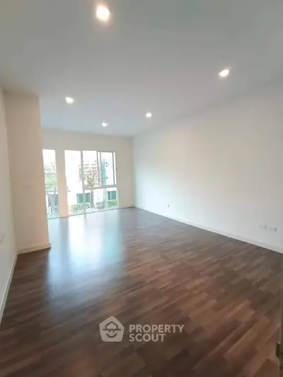 Spacious empty living room with wooden flooring and large windows offering natural light.