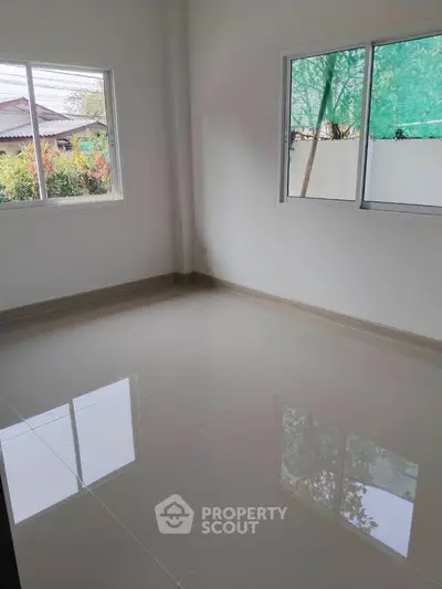 Spacious empty room with glossy tiled floor and large windows offering natural light.