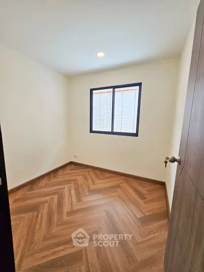 Cozy bedroom with wooden herringbone flooring and natural light from window.