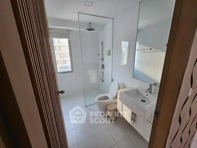 Modern bathroom with glass shower, white fixtures, and natural light.