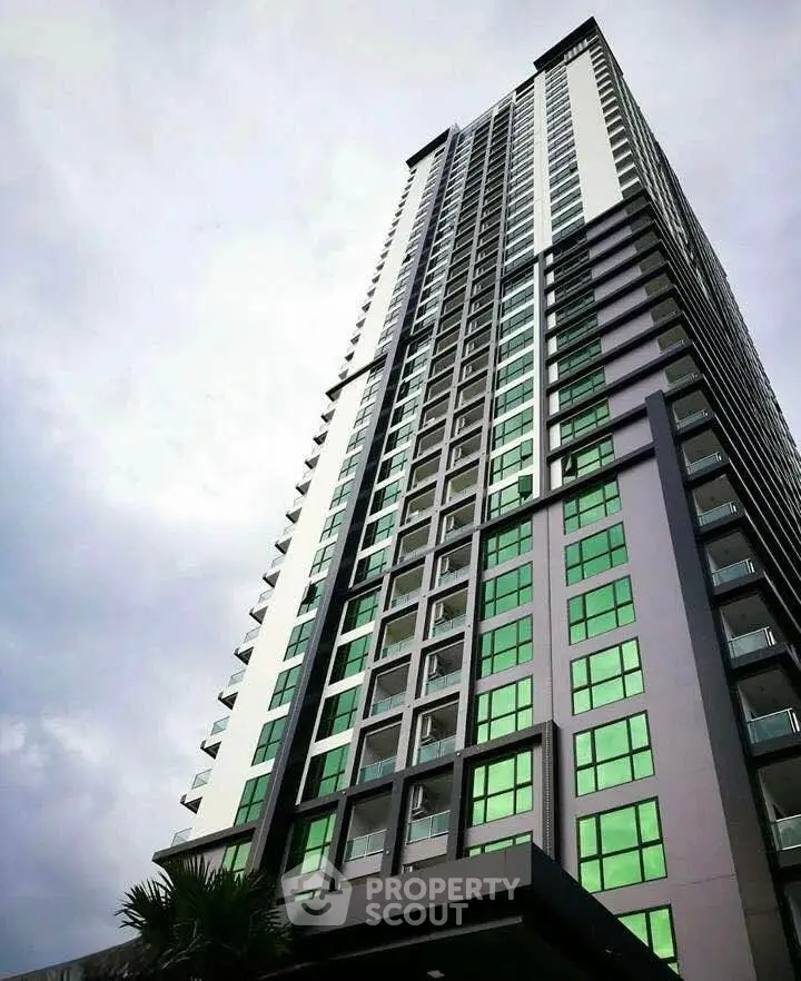 Modern high-rise building with sleek design and green-tinted windows against a cloudy sky.
