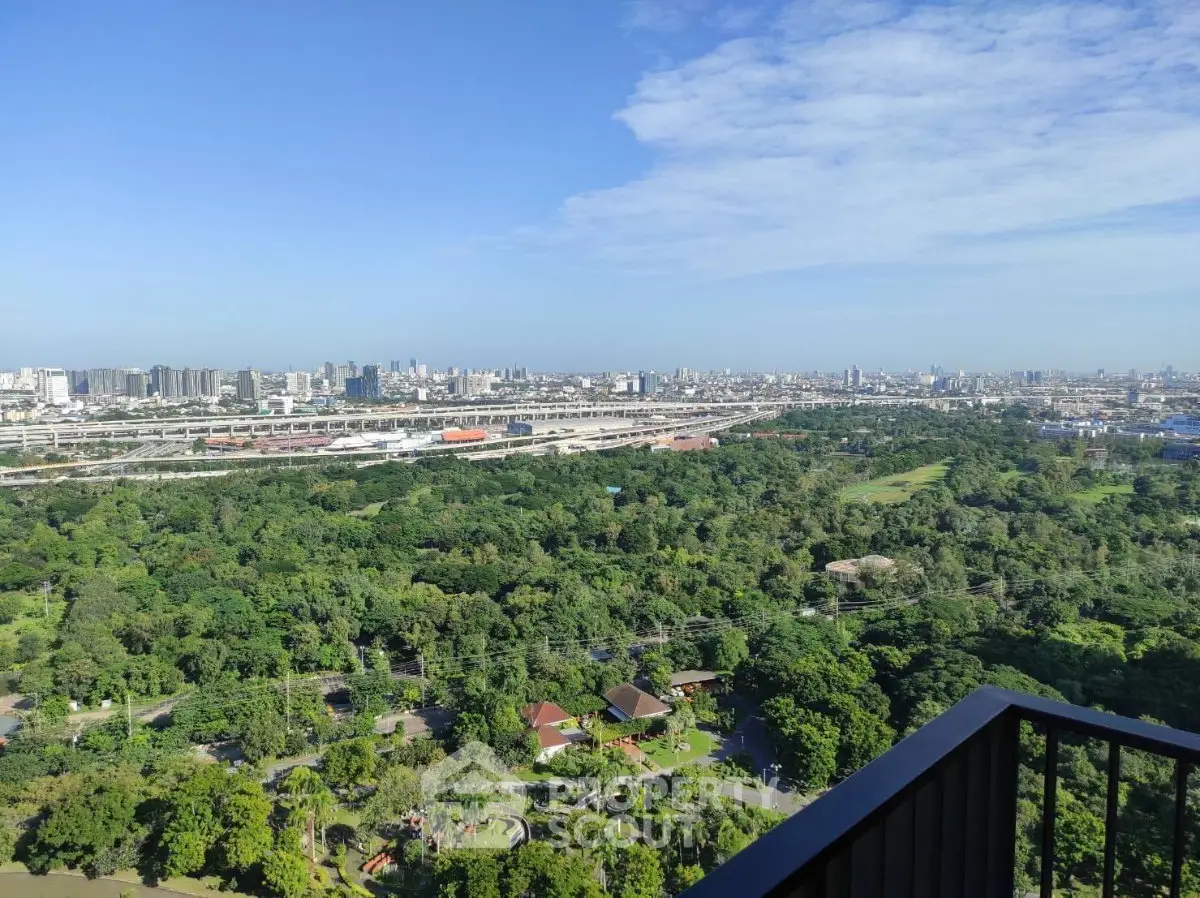Stunning panoramic city view from high-rise balcony overlooking lush greenery and urban skyline.