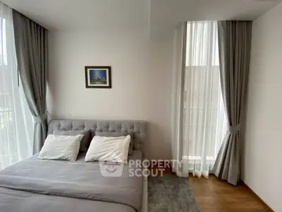 Elegant bedroom with large windows and stylish curtains, featuring a cozy bed and modern decor.