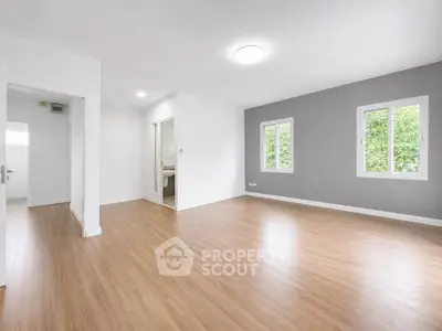 Spacious empty room with wooden flooring and large windows offering natural light.