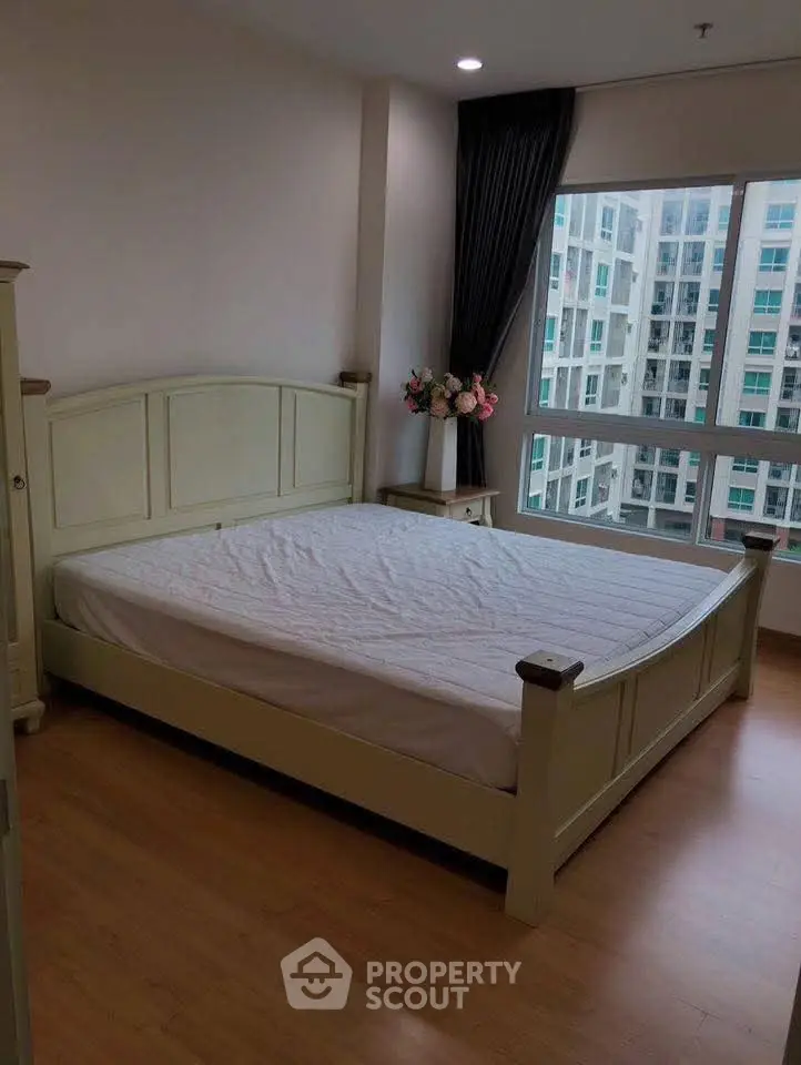Spacious bedroom with large window offering city view in modern apartment.