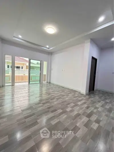 Spacious living room with modern flooring and large windows opening to a balcony.