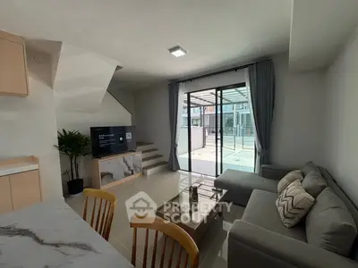 Modern living room with sleek furniture and large glass doors opening to a patio.