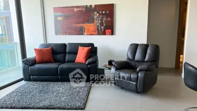 Modern living room with stylish black leather sofa and armchair, accented by red cushions and abstract art.
