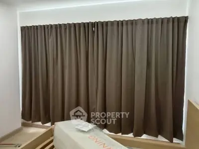 Spacious bedroom with large window and brown curtains, ideal for natural light.