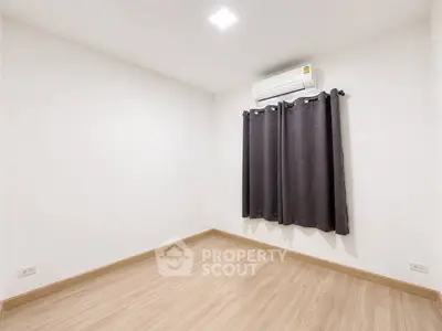 Spacious empty room with wooden flooring and air conditioning, ready for customization.