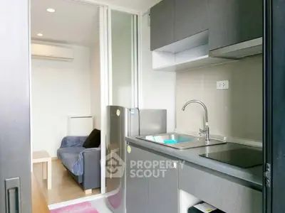Modern compact kitchen with sleek cabinetry and cozy living area in open layout apartment.