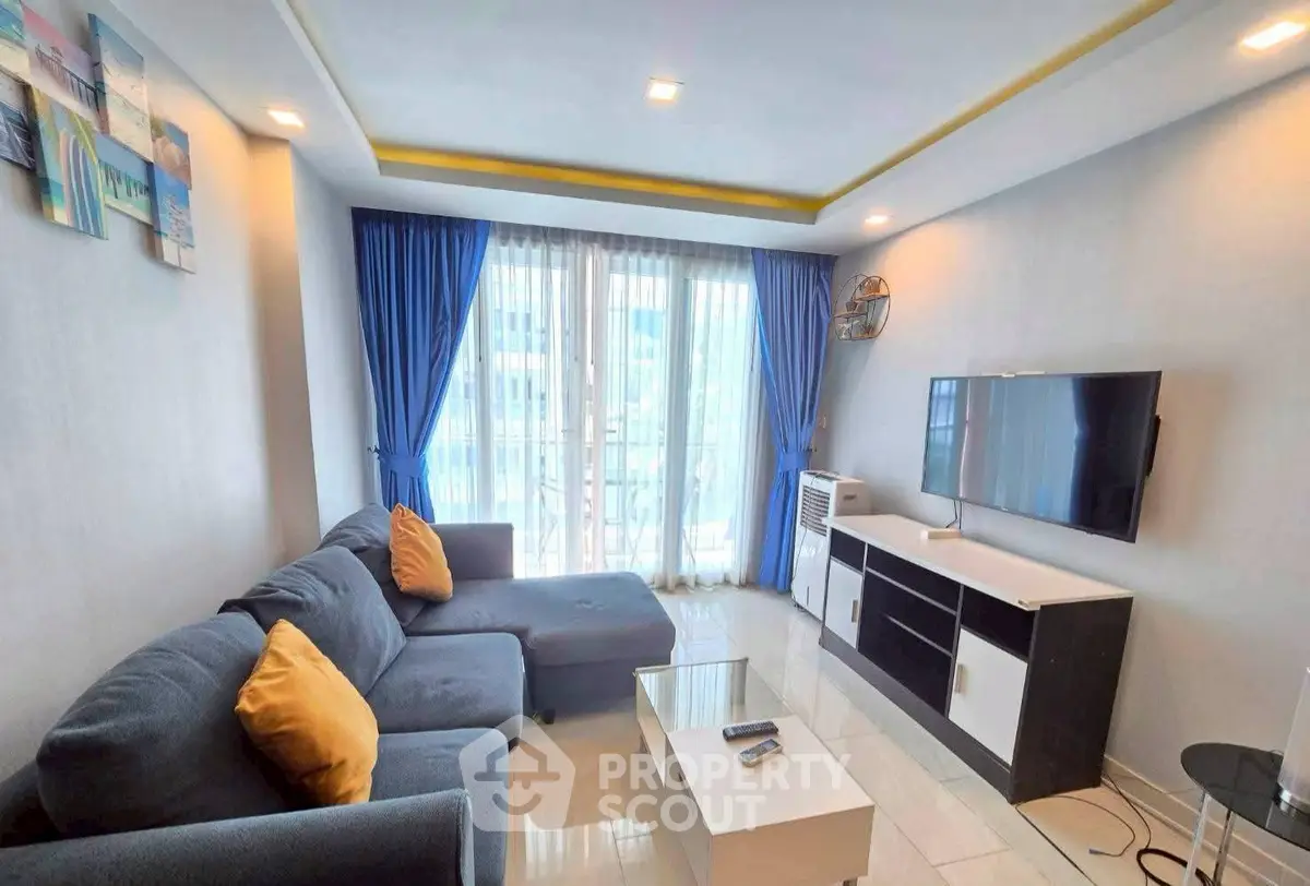 Modern living room with blue curtains, sectional sofa, and wall-mounted TV in a bright apartment.