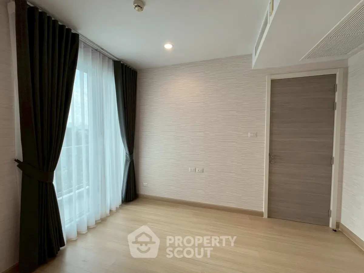 Spacious empty room with wooden flooring and large window with curtains