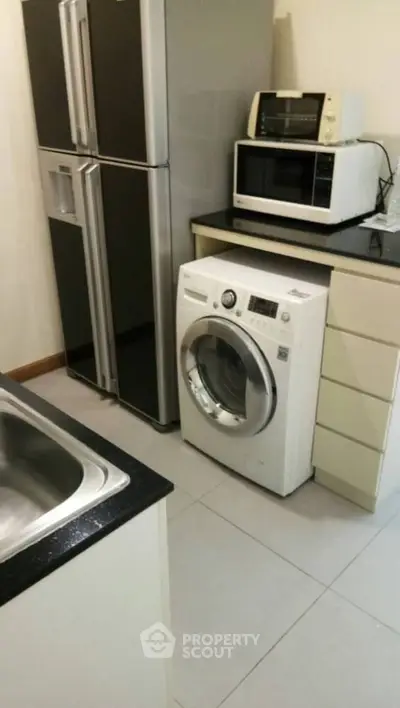 Modern kitchen with washing machine, microwave, and refrigerator in compact layout.