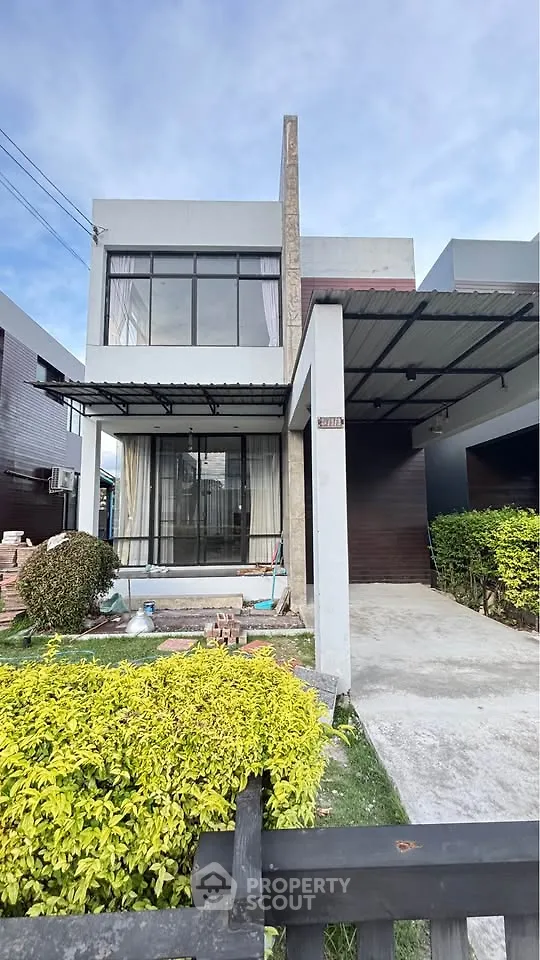 Modern two-story house with large windows and driveway, surrounded by lush greenery.