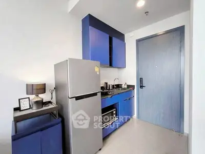Modern compact kitchen with blue cabinets and stainless steel fridge in stylish apartment.