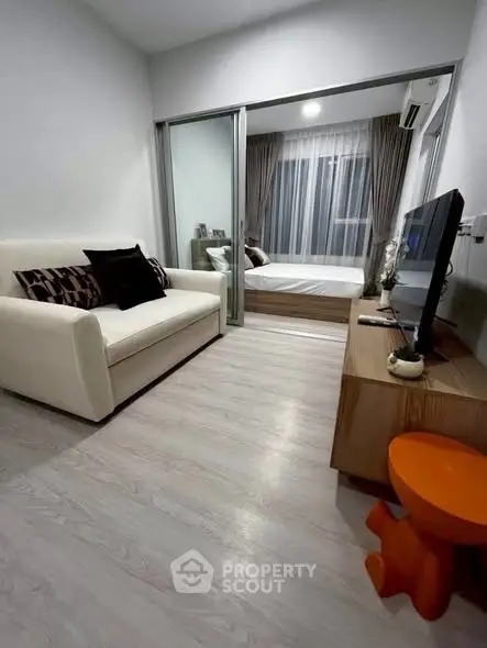 Modern compact living room with cozy sofa and TV, leading to a stylish bedroom through sliding glass doors.