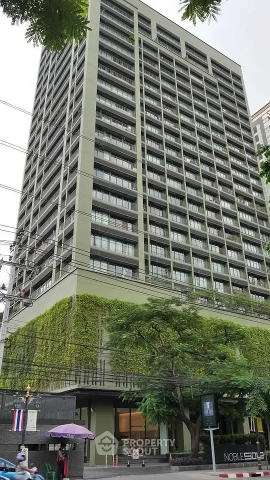 Modern high-rise building with lush greenery on lower floors, showcasing urban living.