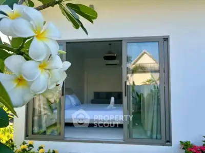 Charming bedroom view through window with lush garden and blooming flowers.