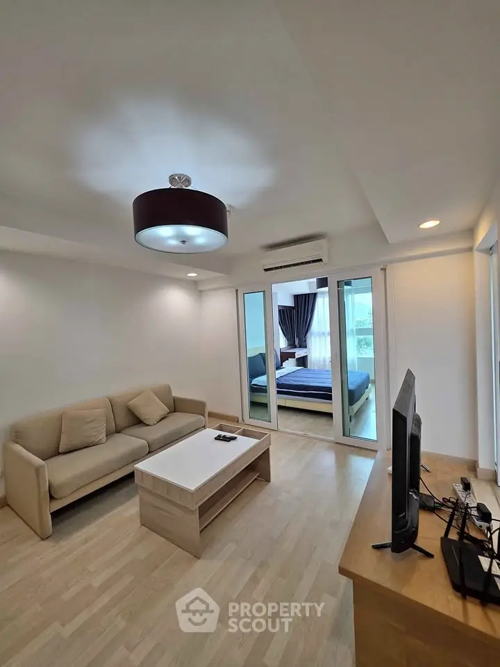 Modern living room with cozy sofa and TV, leading to a stylish bedroom with natural light.