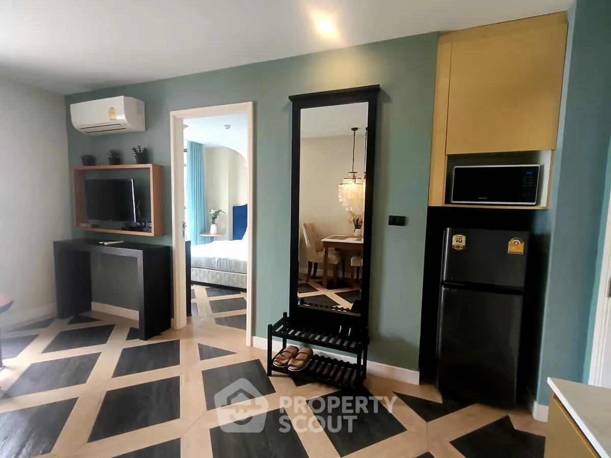 Modern apartment interior with stylish flooring and open layout, featuring a TV, air conditioning, and a glimpse of the bedroom.