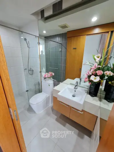 Modern bathroom with glass shower, elegant sink, and floral decor in a stylish apartment.
