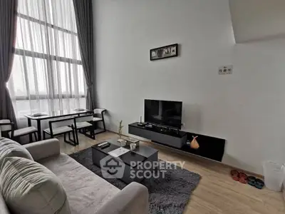 Modern living room with high ceilings and large windows, featuring stylish furniture and a cozy atmosphere.
