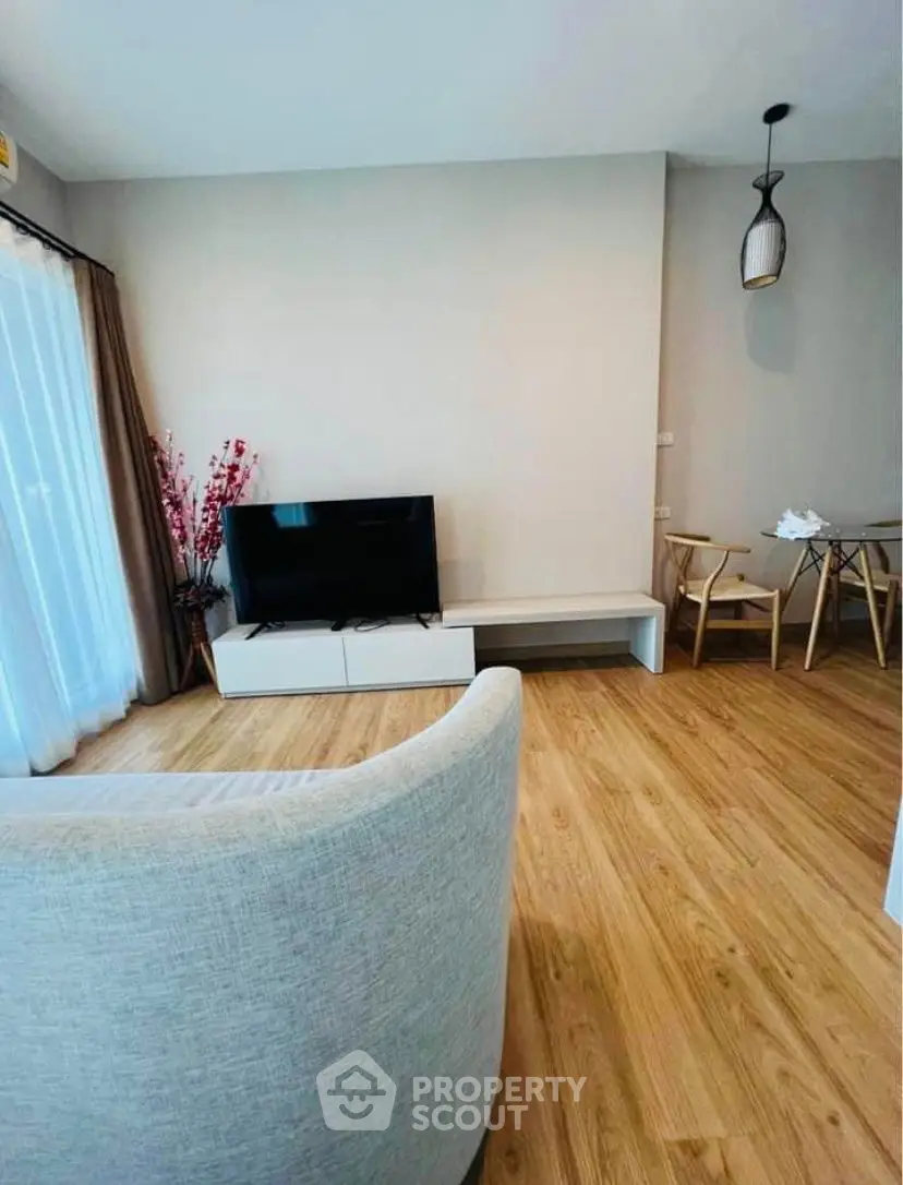 Modern living room with wooden flooring, stylish furniture, and natural light from large windows.