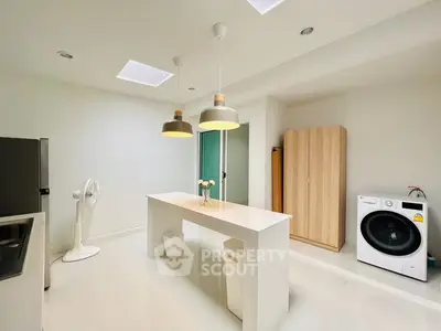 Modern kitchen with sleek island, washing machine, and stylish lighting.