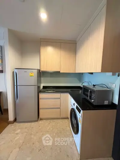 Modern kitchen with fridge, washing machine, and microwave in compact layout.