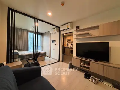 Modern living room with glass partition, cozy bedroom, and sleek kitchen in a stylish apartment.