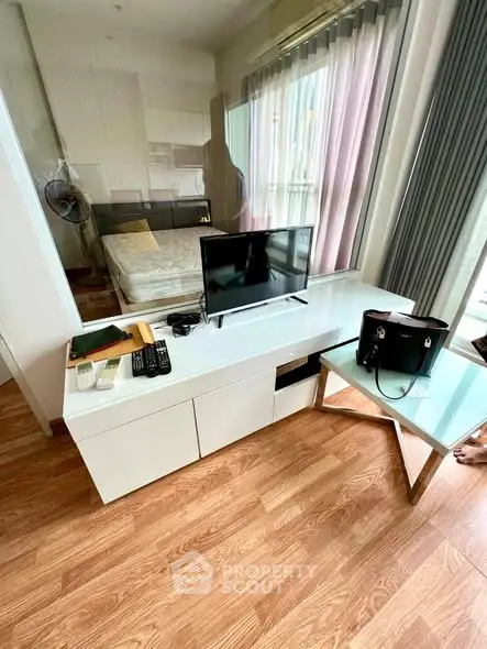 Modern bedroom with sleek TV stand and glass table, featuring wooden flooring and natural light.
