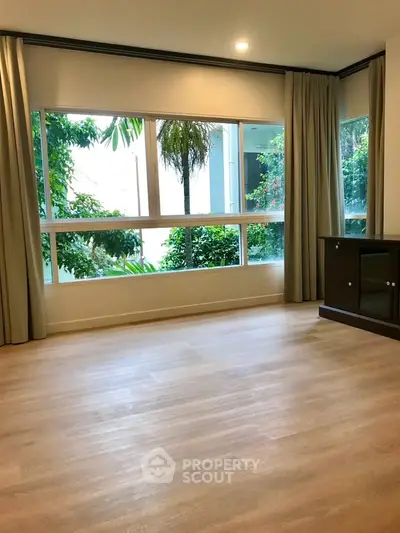 Spacious living room with large windows offering lush garden views, perfect for relaxation and natural light.